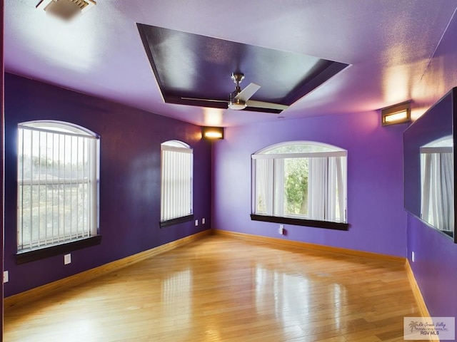 spare room with ceiling fan, a tray ceiling, and light hardwood / wood-style flooring