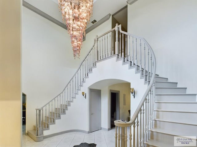 stairs with tile patterned flooring, a notable chandelier, and a towering ceiling