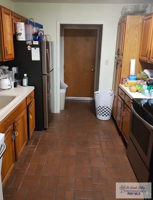 kitchen with light countertops, brown cabinetry, a sink, and stainless steel range with electric stovetop