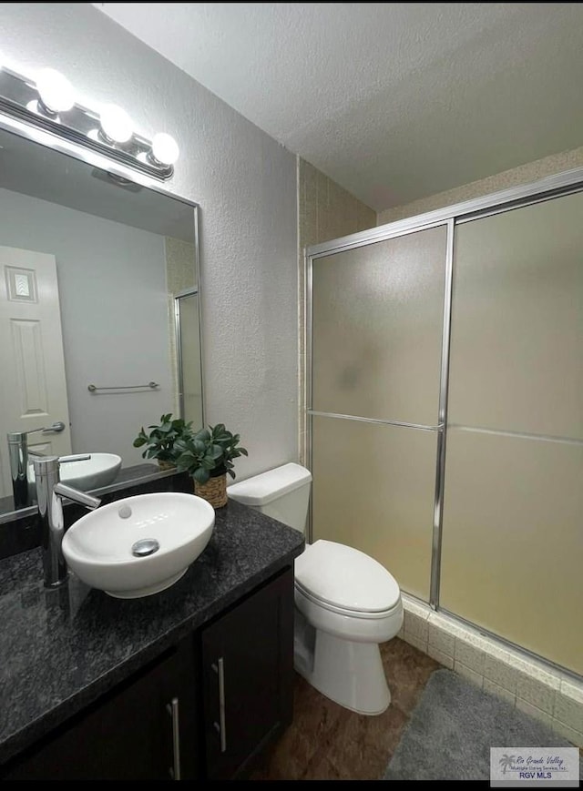 bathroom with vanity, toilet, a shower with shower door, and a textured ceiling