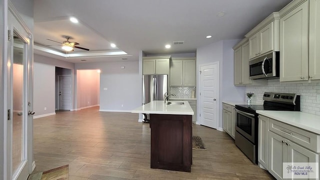 kitchen with ceiling fan, decorative backsplash, a center island with sink, appliances with stainless steel finishes, and hardwood / wood-style flooring