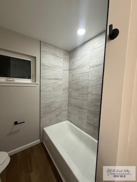 full bath featuring baseboards, bathing tub / shower combination, toilet, and wood finished floors