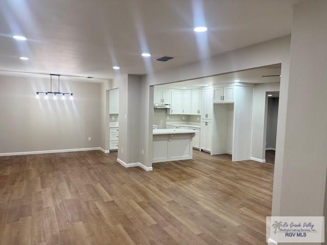 kitchen with under cabinet range hood, wood finished floors, white cabinetry, light countertops, and hanging light fixtures