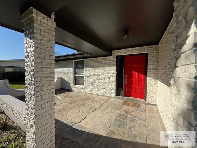 entrance to property featuring a patio and brick siding