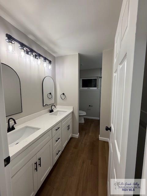 full bath featuring double vanity, a sink, toilet, and wood finished floors