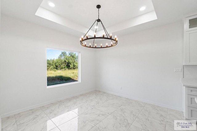 unfurnished dining area with an inviting chandelier and a tray ceiling