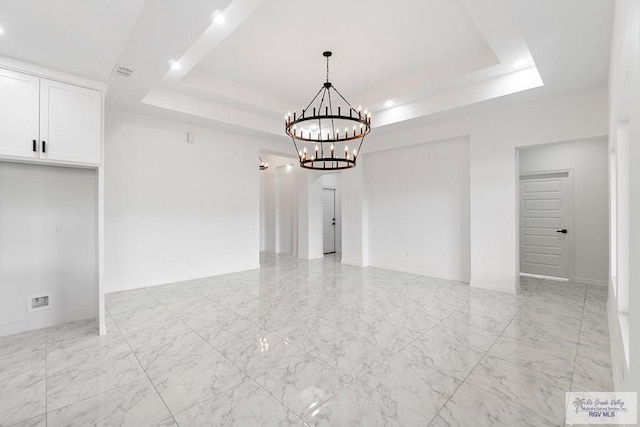 spare room featuring a raised ceiling and an inviting chandelier