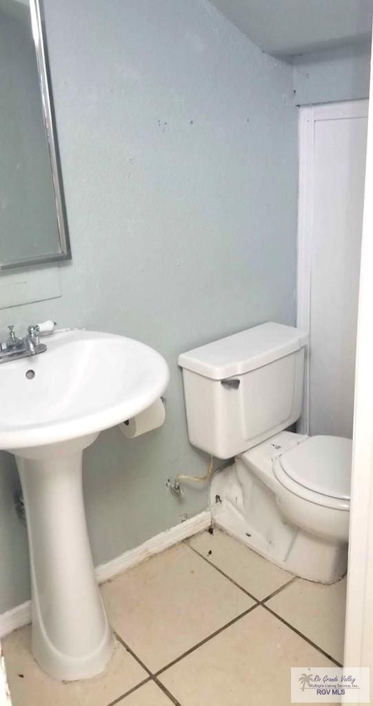 half bathroom with toilet, tile patterned flooring, baseboards, and a sink