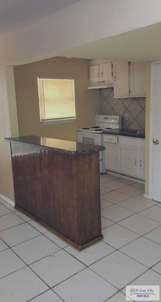 kitchen featuring light tile patterned floors, electric range, dark countertops, under cabinet range hood, and backsplash