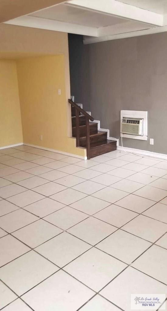 spare room featuring light tile patterned floors, baseboards, beamed ceiling, stairs, and an AC wall unit