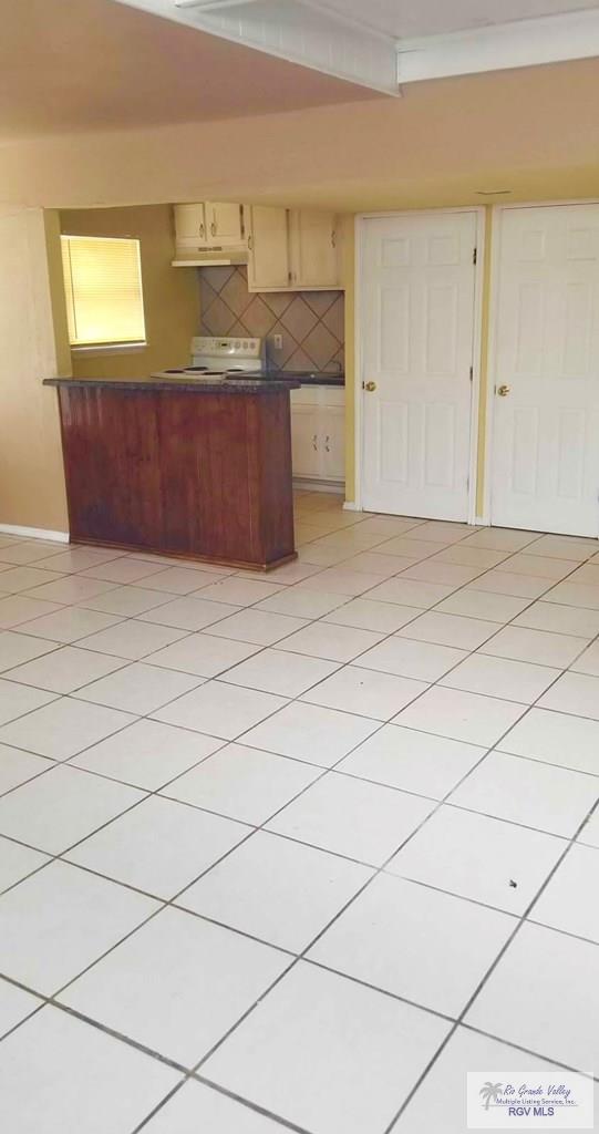 kitchen featuring light tile patterned floors, white electric stove, under cabinet range hood, tasteful backsplash, and dark countertops