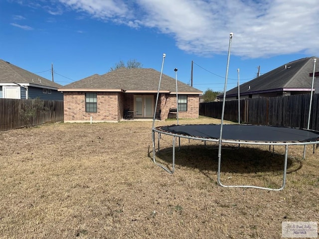 back of house with a trampoline and a yard