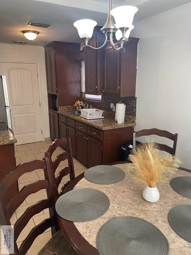 kitchen with sink, backsplash, fridge, light tile patterned flooring, and dark stone counters