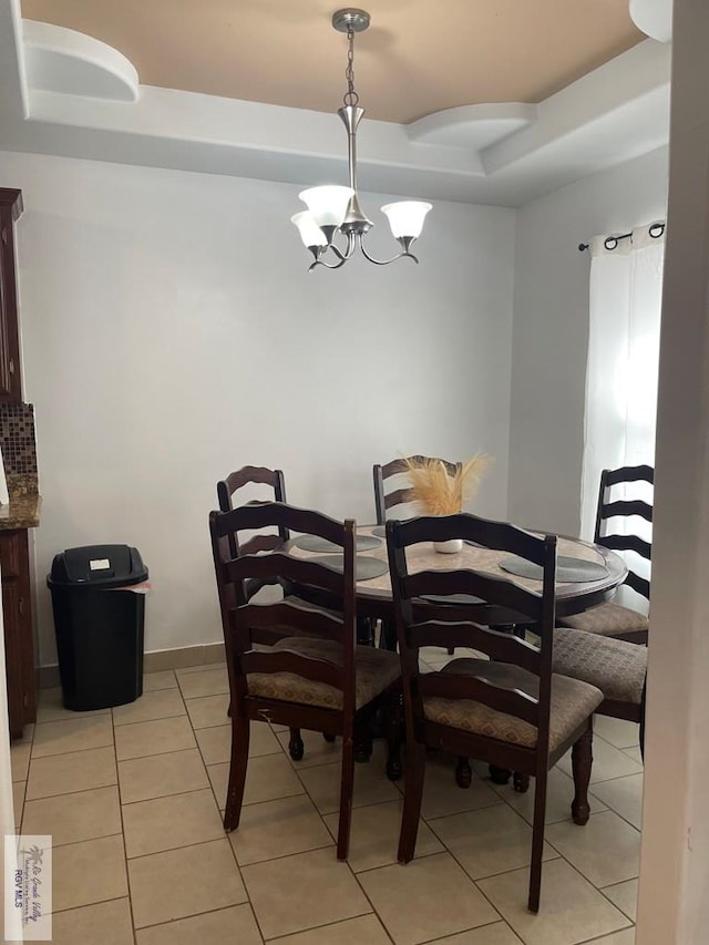 tiled dining room featuring an inviting chandelier and a raised ceiling