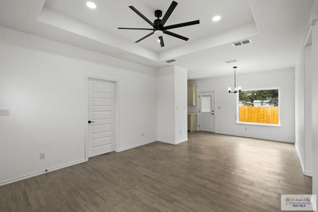 unfurnished living room with ceiling fan with notable chandelier, dark wood-type flooring, and a raised ceiling