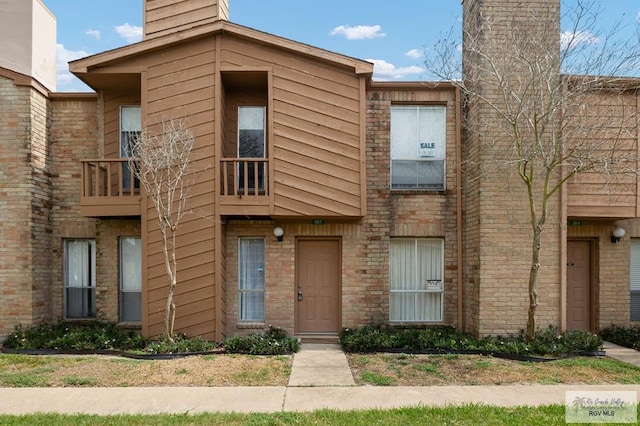 view of property with a balcony, a chimney, and brick siding