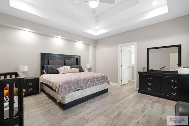 bedroom with a raised ceiling, ceiling fan, and light wood-type flooring