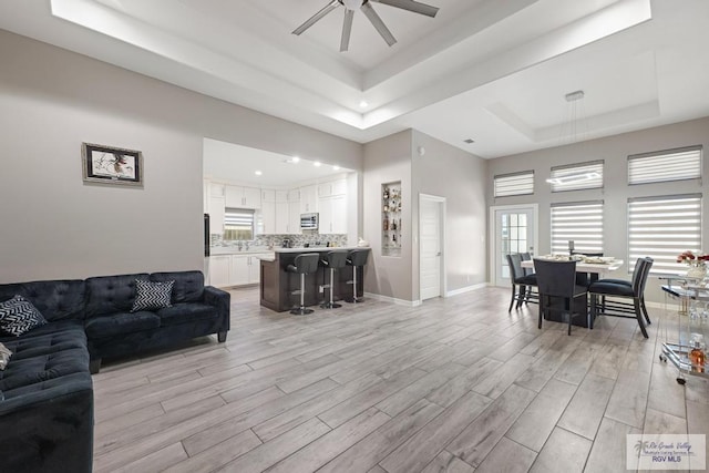 living room with a tray ceiling, ceiling fan, and light hardwood / wood-style floors