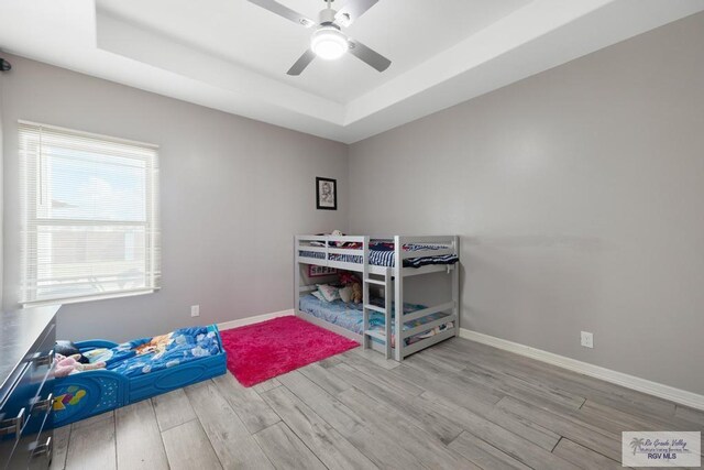 bedroom with ceiling fan, a tray ceiling, and light hardwood / wood-style flooring