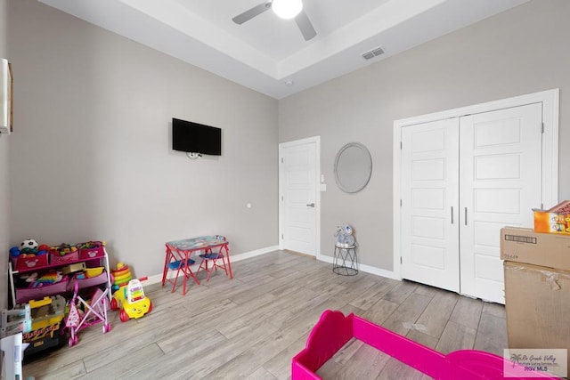 playroom with light hardwood / wood-style floors, ceiling fan, and a tray ceiling