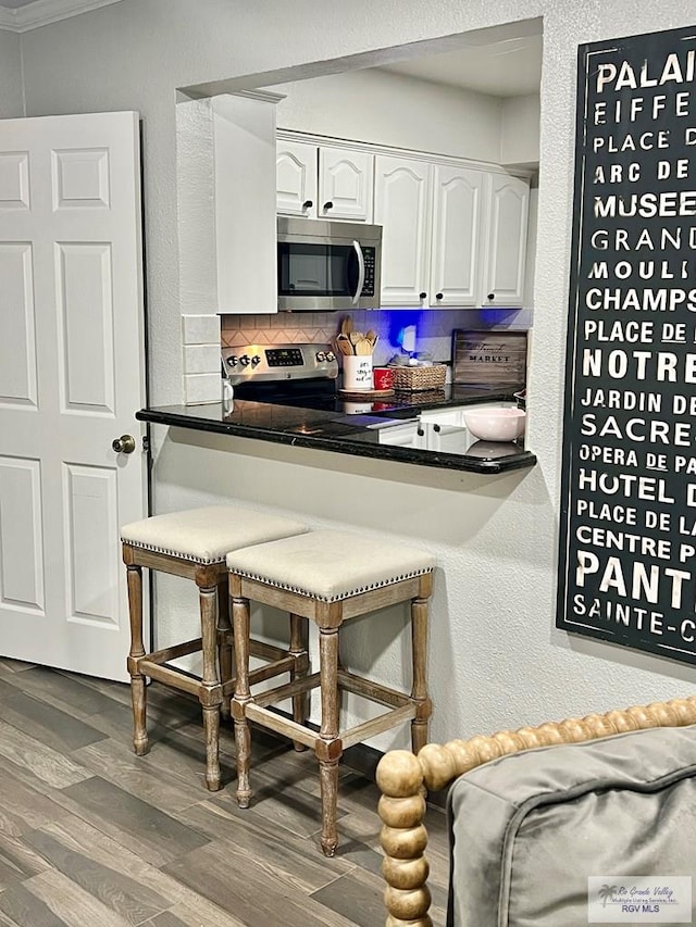 kitchen featuring white cabinets, a kitchen bar, stainless steel appliances, backsplash, and hardwood / wood-style flooring