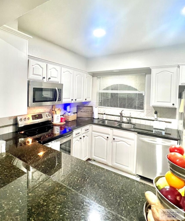 kitchen with dark stone counters, a sink, stainless steel appliances, white cabinetry, and backsplash