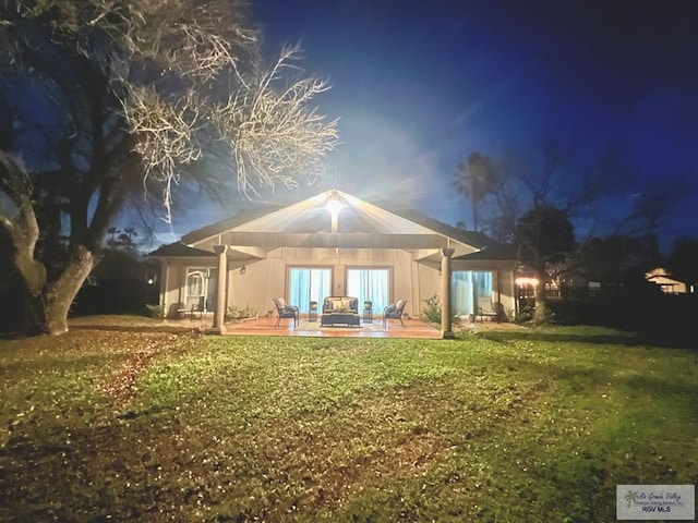 back of house at night with a patio area and a lawn