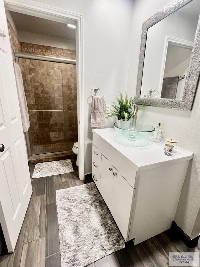 full bath featuring a stall shower, vanity, toilet, and wood finished floors