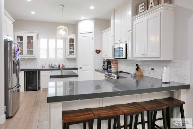 kitchen with a breakfast bar area, light wood-type flooring, decorative light fixtures, kitchen peninsula, and stainless steel appliances