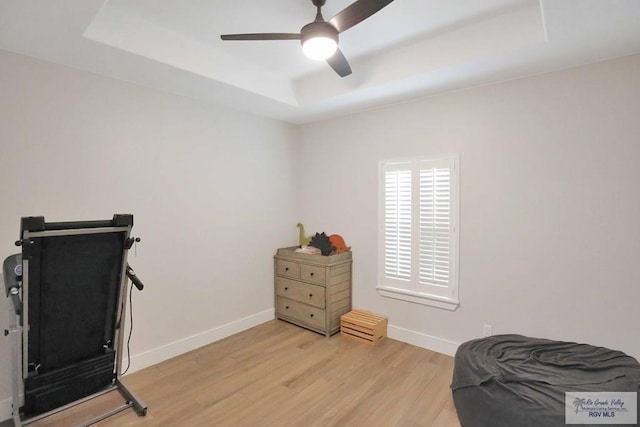 exercise area with light hardwood / wood-style floors, a raised ceiling, and ceiling fan