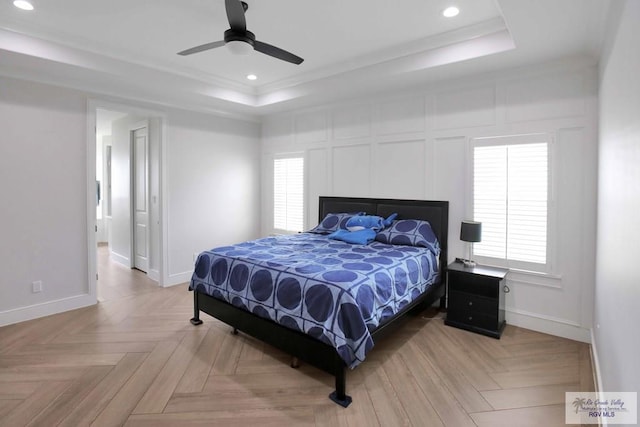 bedroom with ceiling fan, a raised ceiling, light parquet flooring, and multiple windows