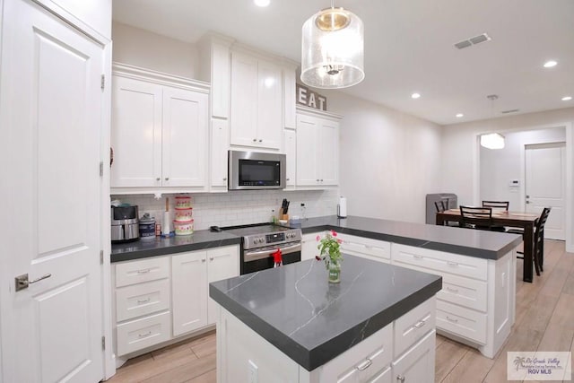 kitchen with white cabinets, decorative light fixtures, a center island, and stainless steel appliances