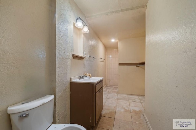 full bath with a textured wall, vanity, toilet, and tile patterned floors