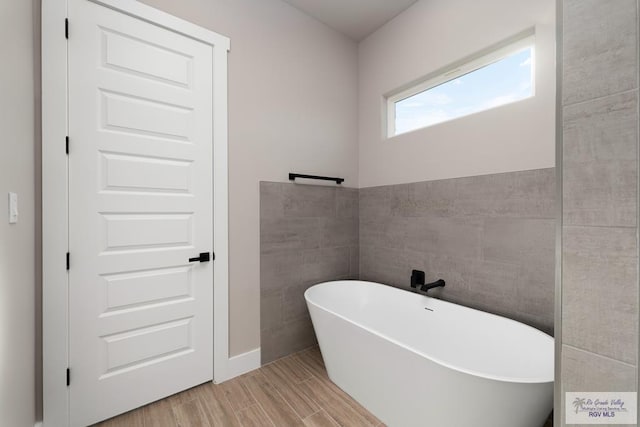 bathroom with a washtub, hardwood / wood-style floors, and tile walls