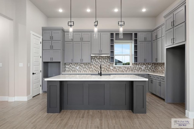 kitchen with pendant lighting, a center island with sink, and gray cabinetry