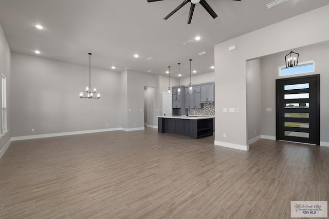 unfurnished living room featuring wood-type flooring, ceiling fan with notable chandelier, and sink