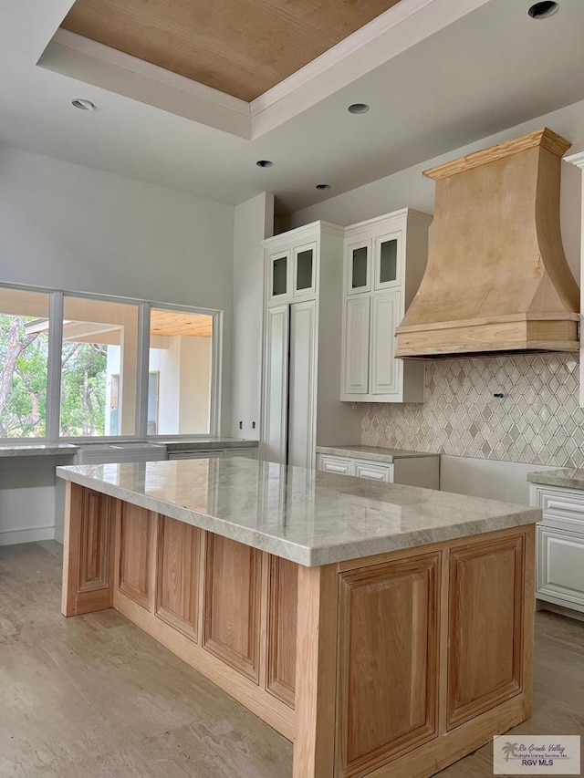 kitchen with backsplash, custom exhaust hood, a raised ceiling, white cabinetry, and a large island