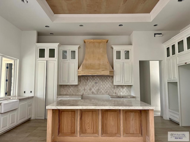 kitchen with a large island, custom range hood, ornamental molding, and a tray ceiling