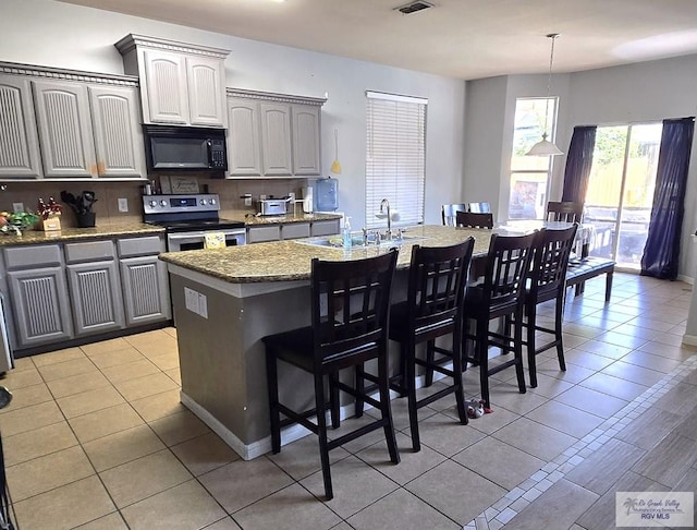 kitchen featuring gray cabinetry, a breakfast bar, a kitchen island with sink, electric stove, and light tile patterned flooring