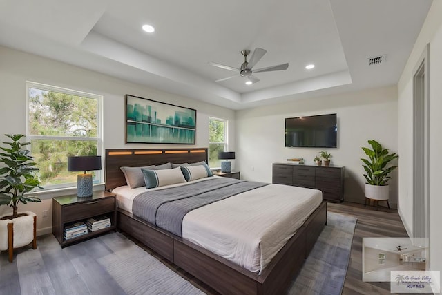 bedroom with dark wood-type flooring, ceiling fan, and a raised ceiling