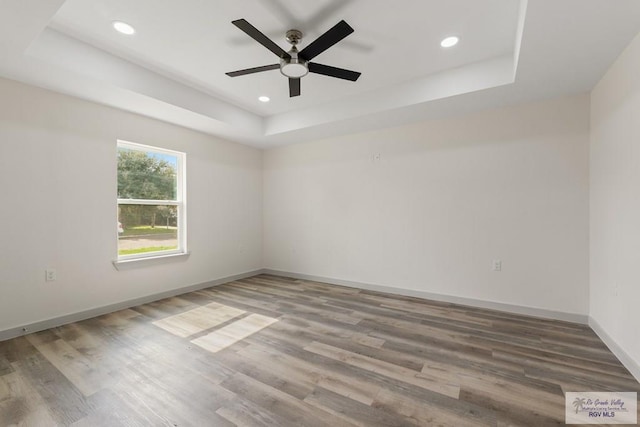 spare room with a tray ceiling, ceiling fan, and hardwood / wood-style flooring