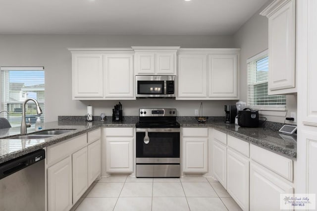 kitchen with appliances with stainless steel finishes, white cabinets, a sink, and light tile patterned flooring