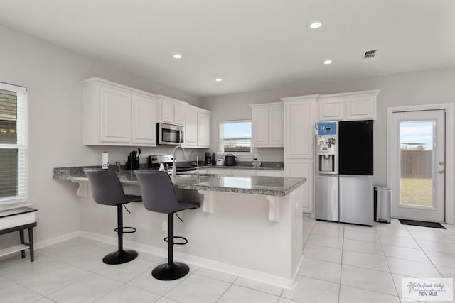 kitchen with stainless steel appliances, white cabinetry, a breakfast bar area, and light tile patterned floors