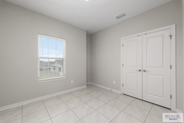 unfurnished bedroom featuring a closet, light tile patterned flooring, visible vents, and baseboards