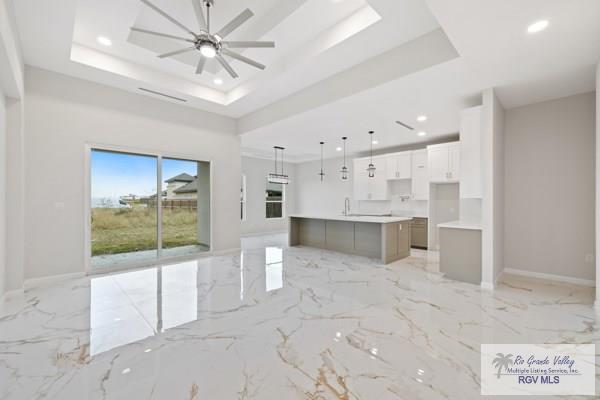 unfurnished living room with marble finish floor, a tray ceiling, a ceiling fan, and baseboards