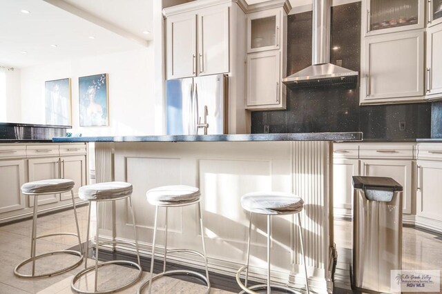 kitchen with white cabinets, wall chimney range hood, stainless steel fridge, and backsplash