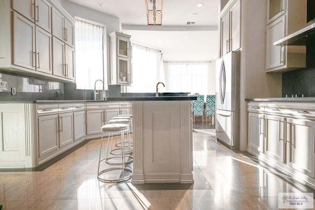 kitchen featuring stainless steel refrigerator, tasteful backsplash, extractor fan, an island with sink, and a kitchen bar