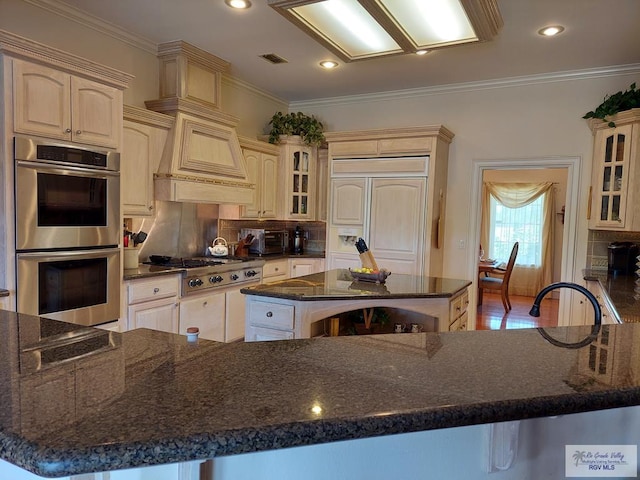 kitchen with a center island, dark stone countertops, ornamental molding, tasteful backsplash, and stainless steel appliances