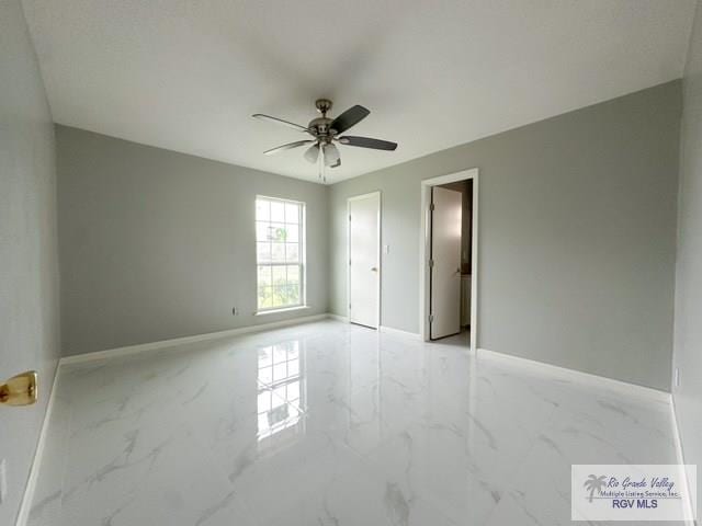 empty room featuring marble finish floor, a ceiling fan, and baseboards