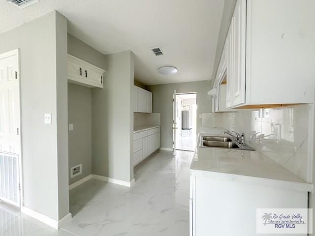 kitchen with marble finish floor, decorative backsplash, white cabinets, a sink, and baseboards